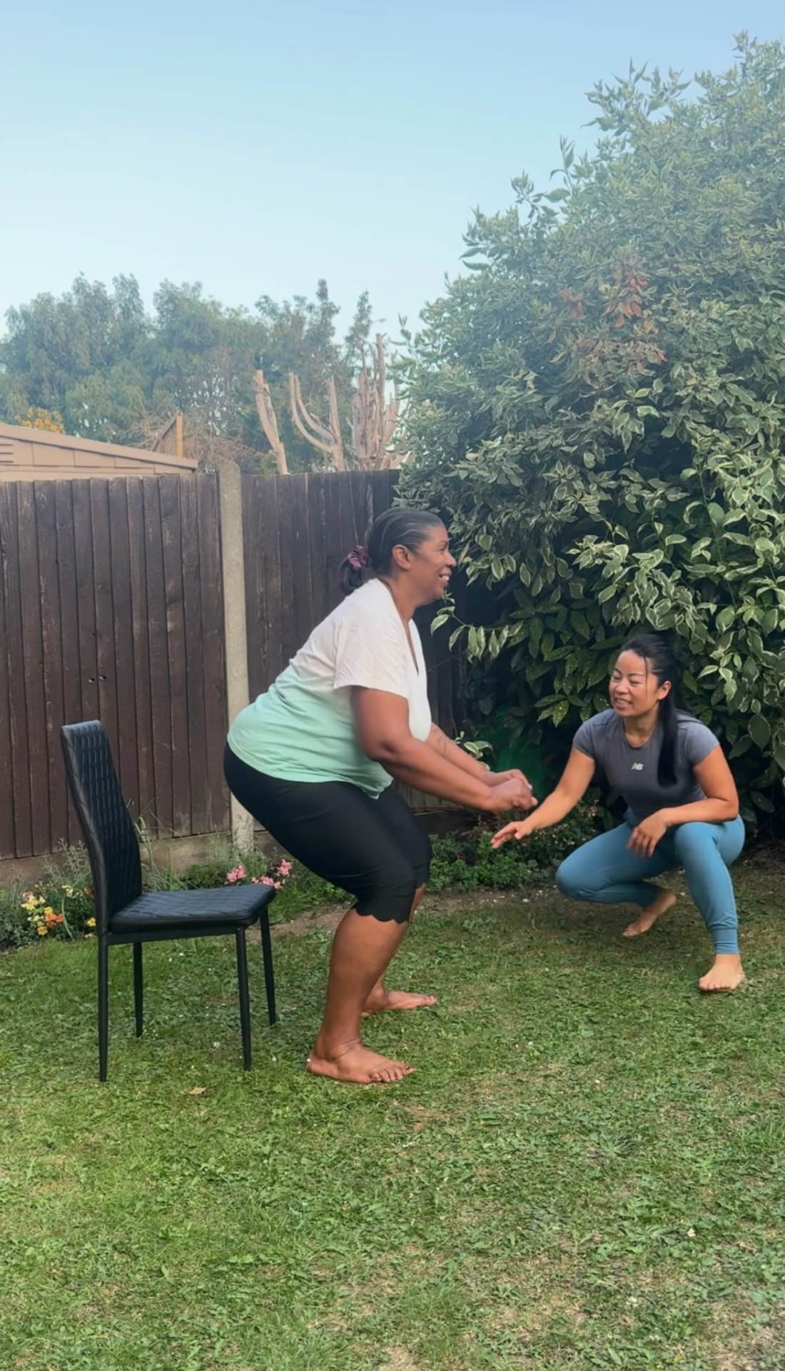 Client practising a chair stand exercise in the garden with coach Ao guiding her