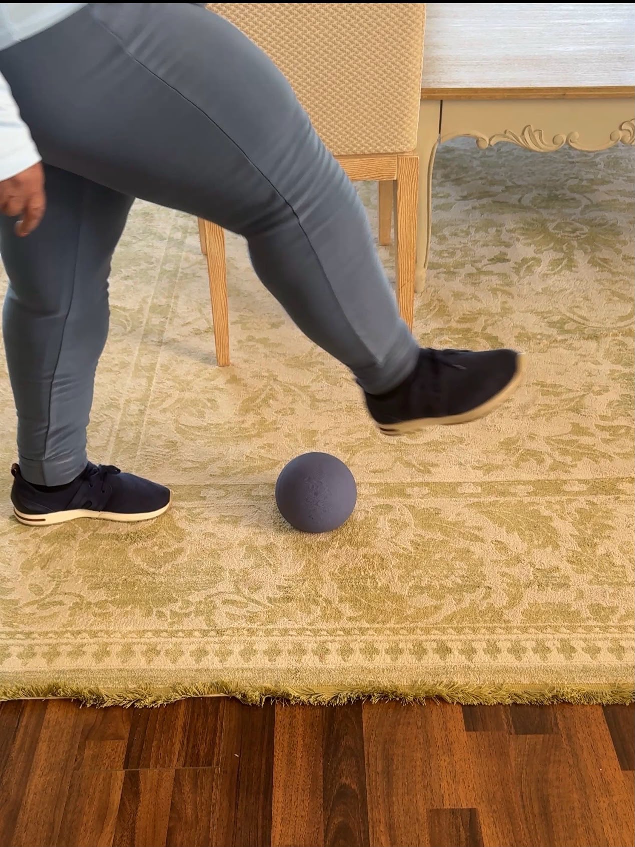 Client performing a balance and coordination drill with a small ball at home